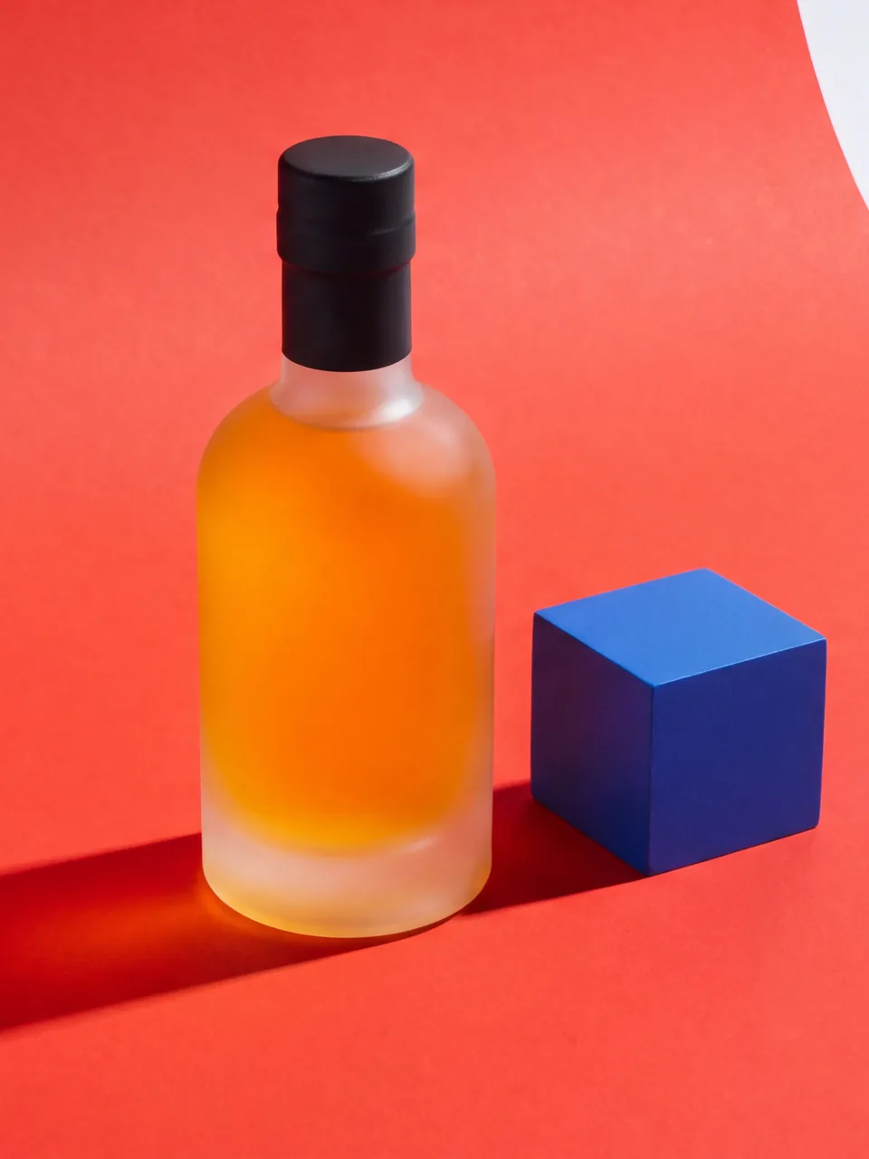Colour-block studio: an amber bottle on red with one hard shadow
